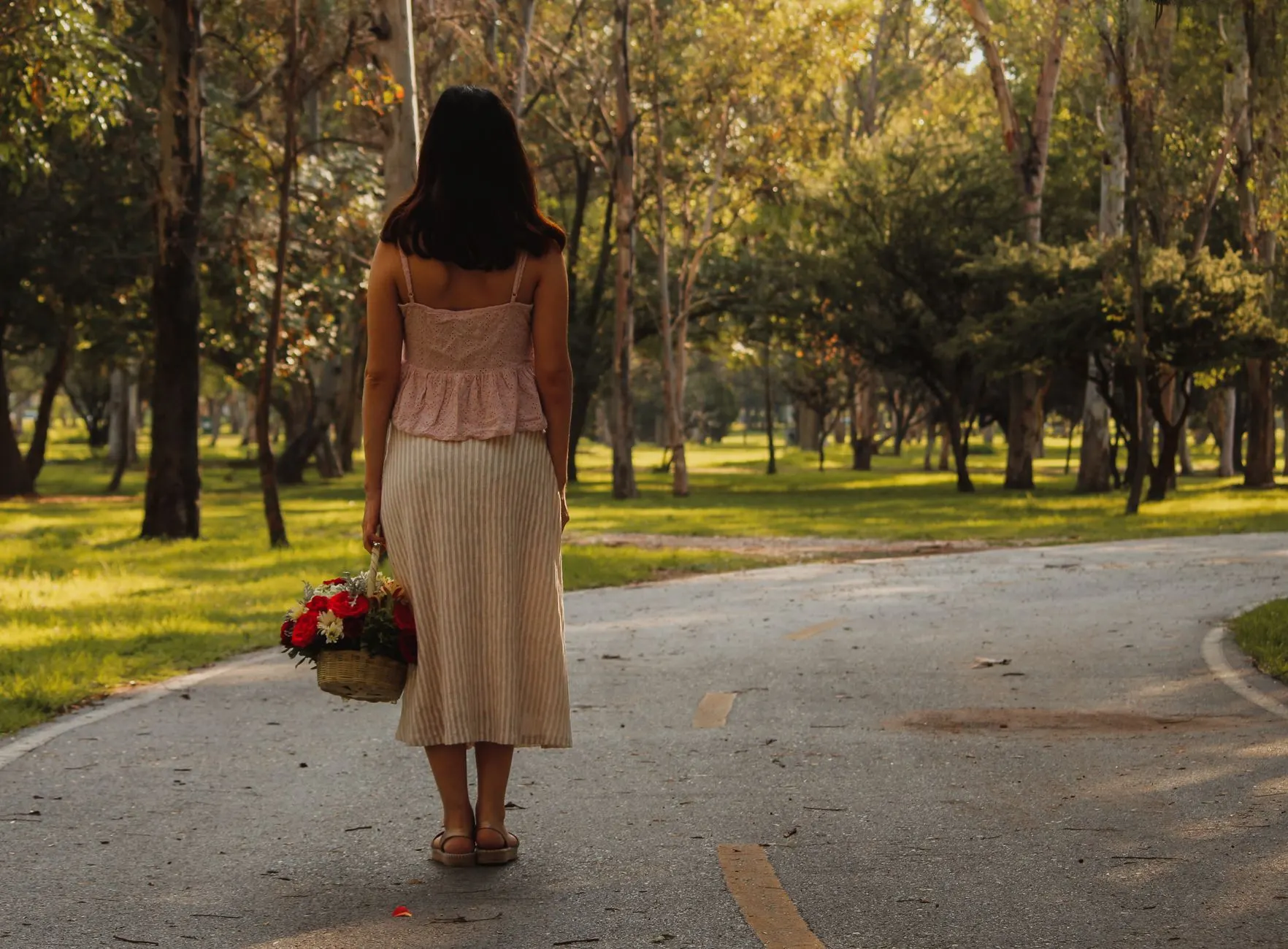 Woman in a pink eyelet top and striped midi skirt walking through a sunlit park