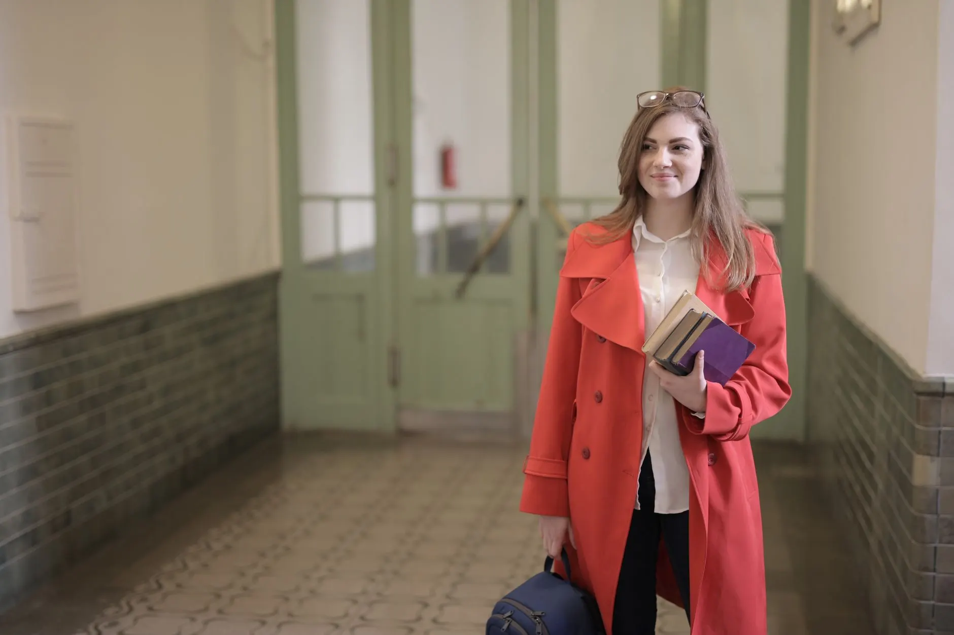 Teen in an orange trench coat and trousers carrying books, a smart-casual school outfit