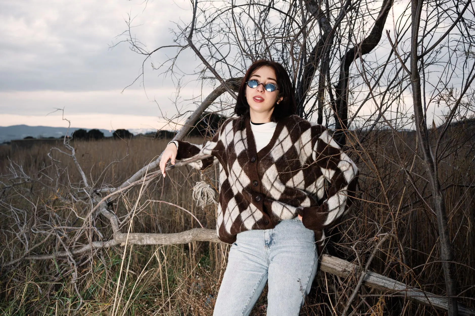 Teen in a Y2K-inspired argyle cardigan, jeans, and round sunglasses