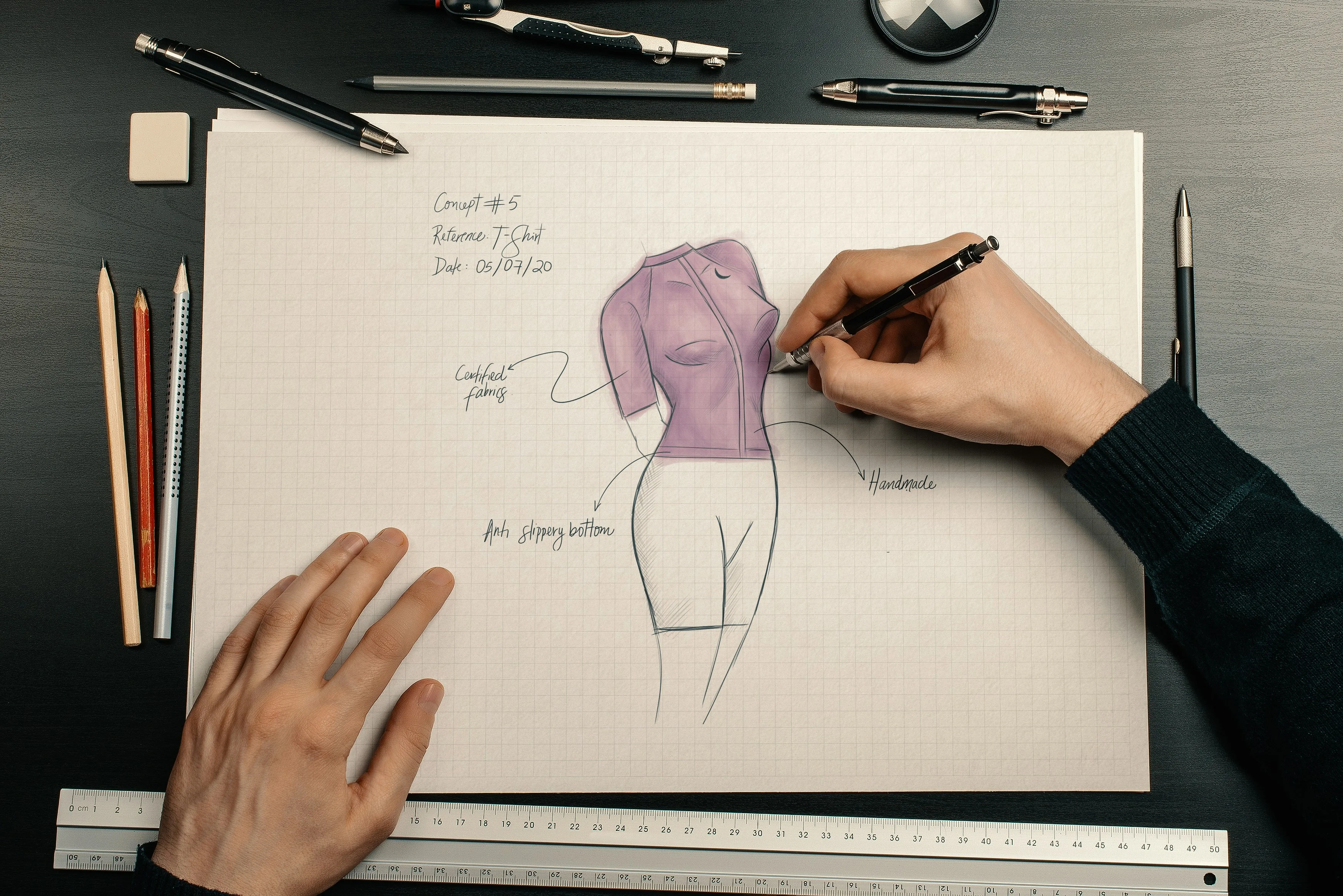 Fashion sketch of a garment silhouette on grid paper, being measured and annotated by hand with a ruler